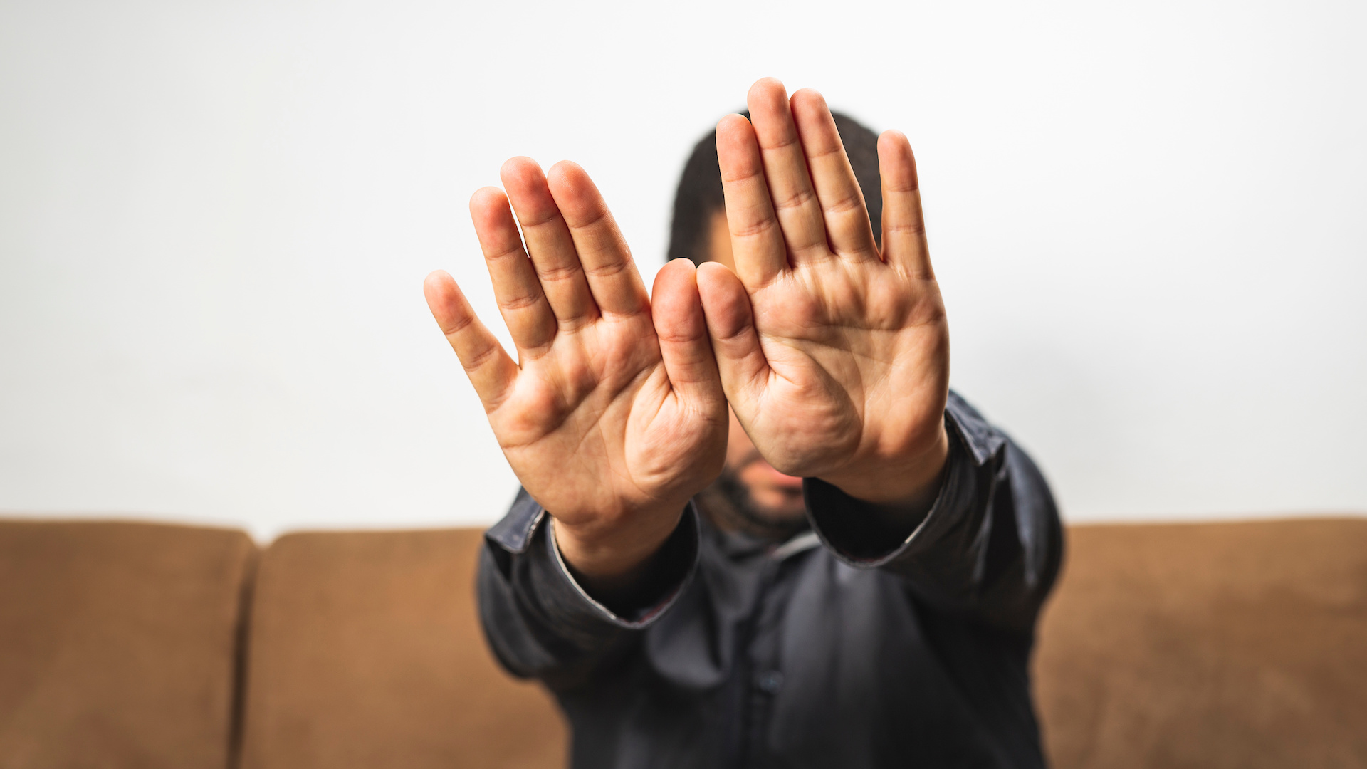 Serious Young Man Sitting On Sofa And Showing Stop Gesture Hand Gesture Hide Face Stop Sign
