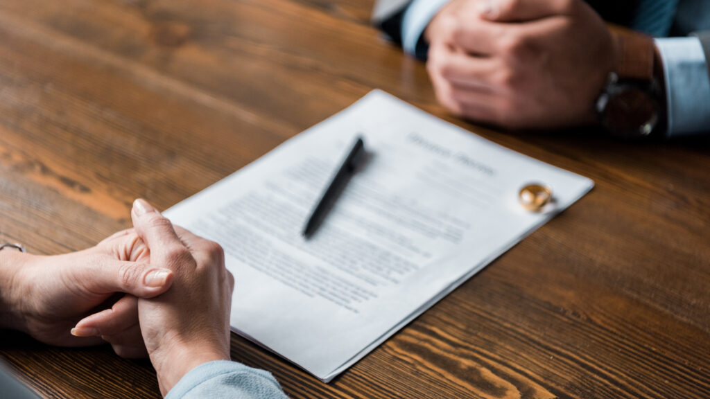 Partial View Of Lawyer And Client Sitting At Table With Divorce Decree And Wedding Rings
